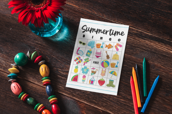 desk background with crayons and flower with bingo card ready to play pool party themed bingo with shells, flip flops, pineapple, water gun and more