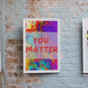 Framed You Matter poster on a brick background