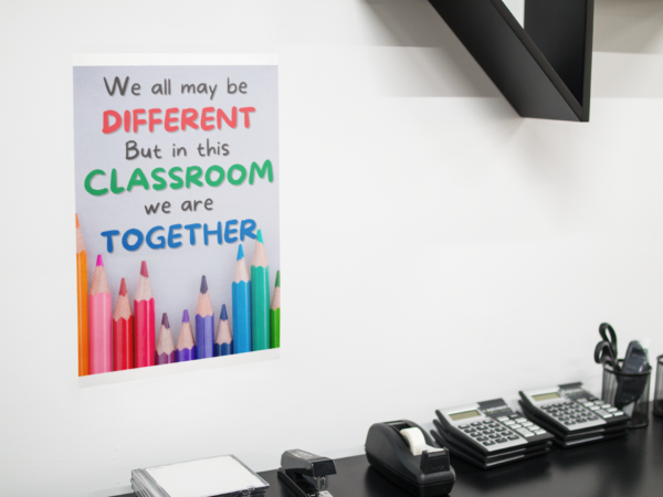 In This Classroom We Are Together poster on a white wall over a desk