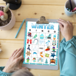 Senior sitting at a table with arms and part of her head shown with clipboard with Winter BINGO displayed ready to play