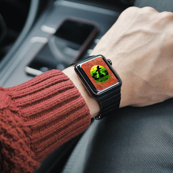 person arm sitting in a car with red sweater and arm on knee, watch is black with orange background wash with yellow green circle, mamasarsus rex, three scratch marks, and one black dino with red heart and two little dinos that are green