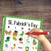 wood table with green dot background with st Patrick's day bingo with images of the green holiday with young childs hand over the bingo card