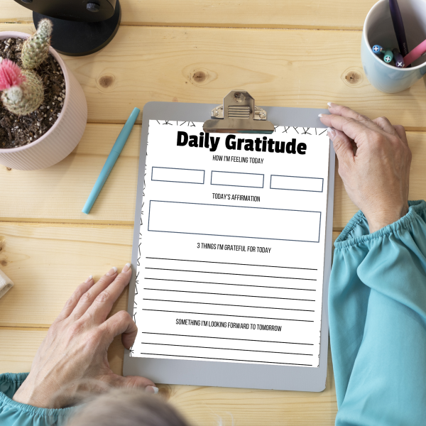 blond wood table with pen and clipboard holding daily gratitude sheet