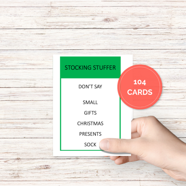 white wood table with hand holding one card thats already cut out with Stocking Stuffer in green bar, then Don't Say Small, Gifts, Christmas, Presents, Sock, circle saying 104 cards