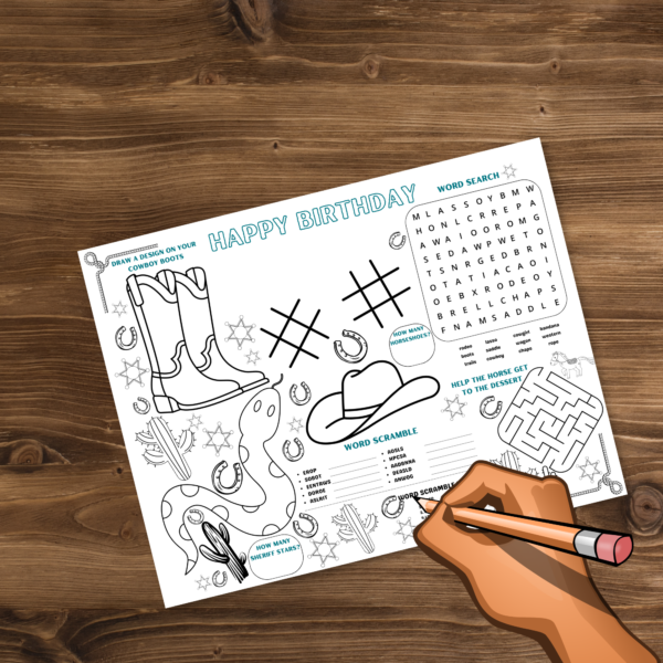 desk with hand holding pencil ready to fill out the personalized western happy birthday placemat word scramble activity. maze, word search an play tic tac toe