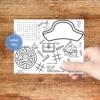 brown table with hand holding the pirate activity placemat with design your pirate hat, word search, maze, looking glass count, tic tac toe, word scramble, and speak like a pirate, and you can color the images too.Blue circle LETTER SIZE