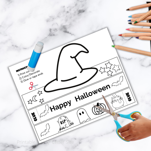 white marble table, colored, pencils, glue stick, and hands ready with scissors ready to cut out the witch hat headband crown with stars, Happy Halloween,bats, ghost, pumpkins on it. Instructions say, print out, color, glue or tape each ends.