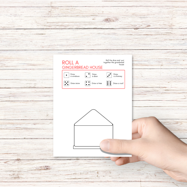 white wood table, shows hand holding the roll a gingerbread house with red box with dice showing what to do for each dice roll.